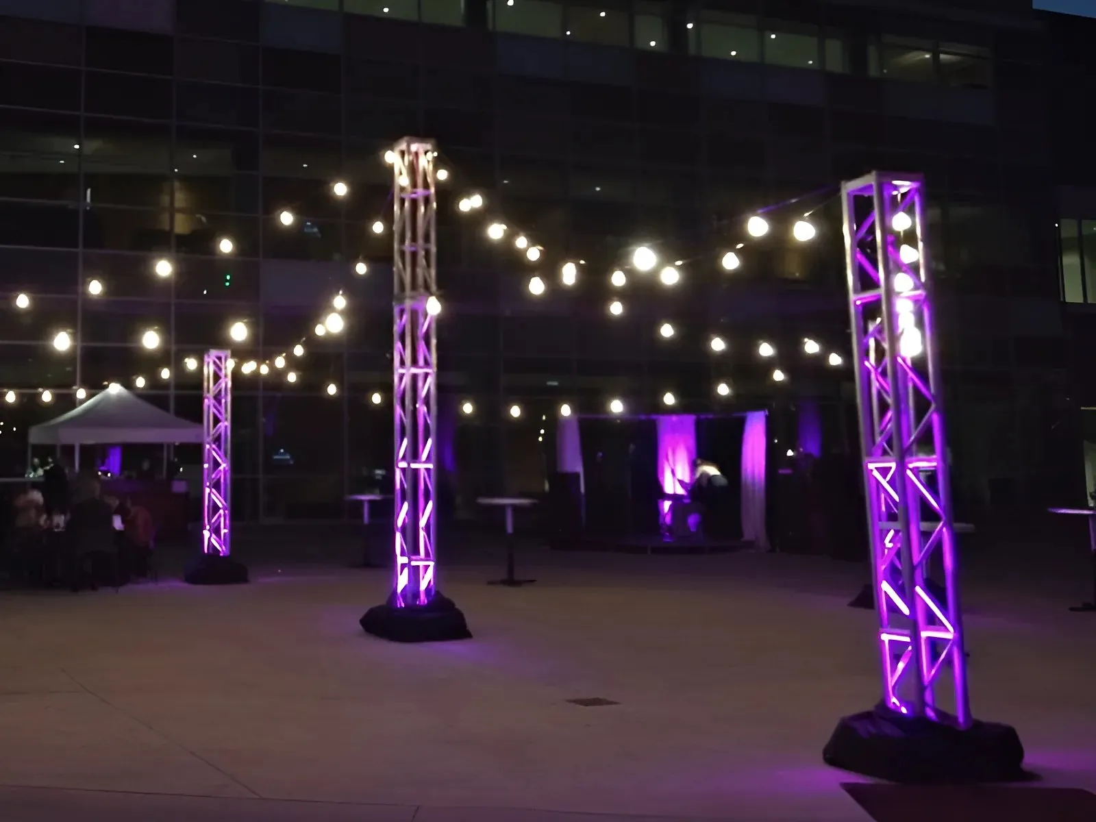 Festoon lighting strung from lit truss towers at dusk