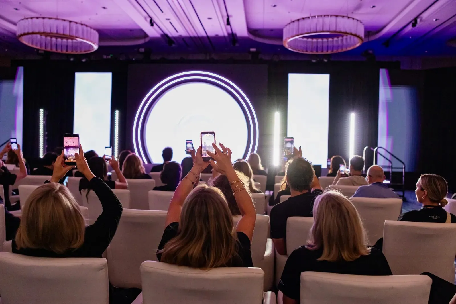 Audience photographing the main stage at a corporate program
