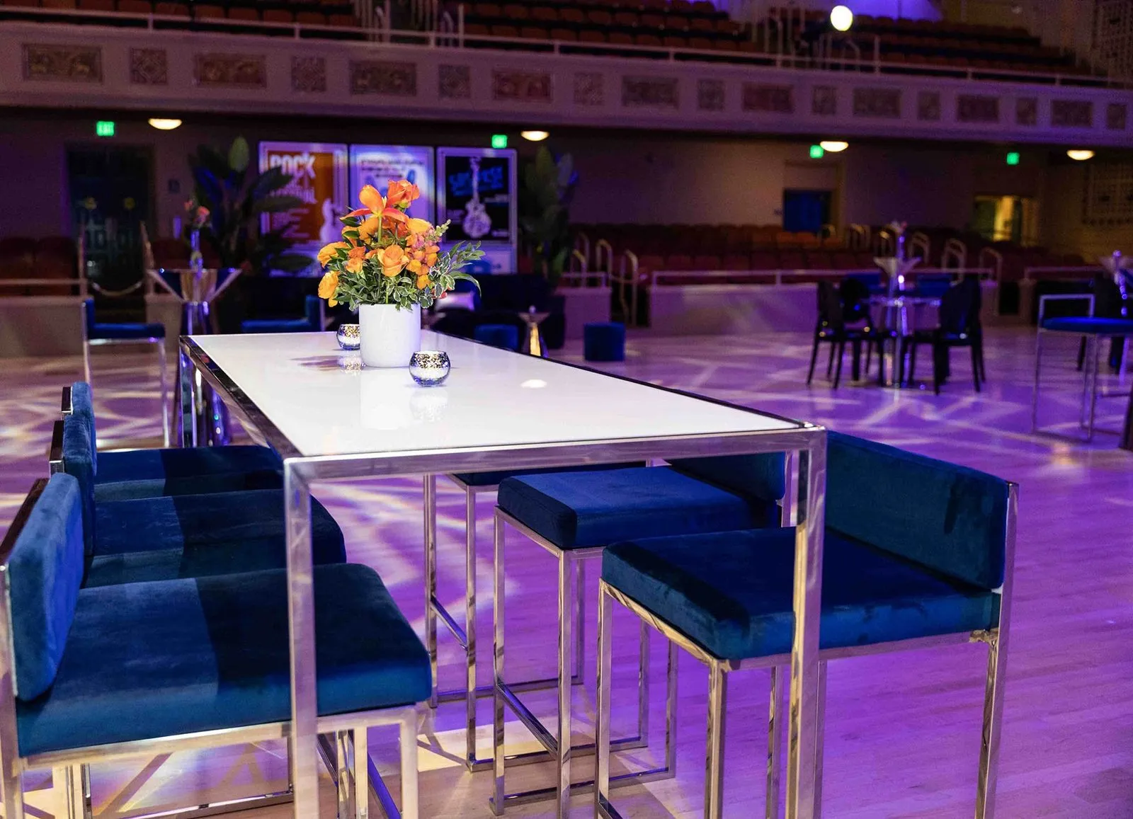 Lounge furniture and a long table under purple lighting in a large event hall