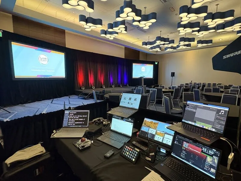 Front-of-house tech table with laptops and control surfaces facing a general session stage