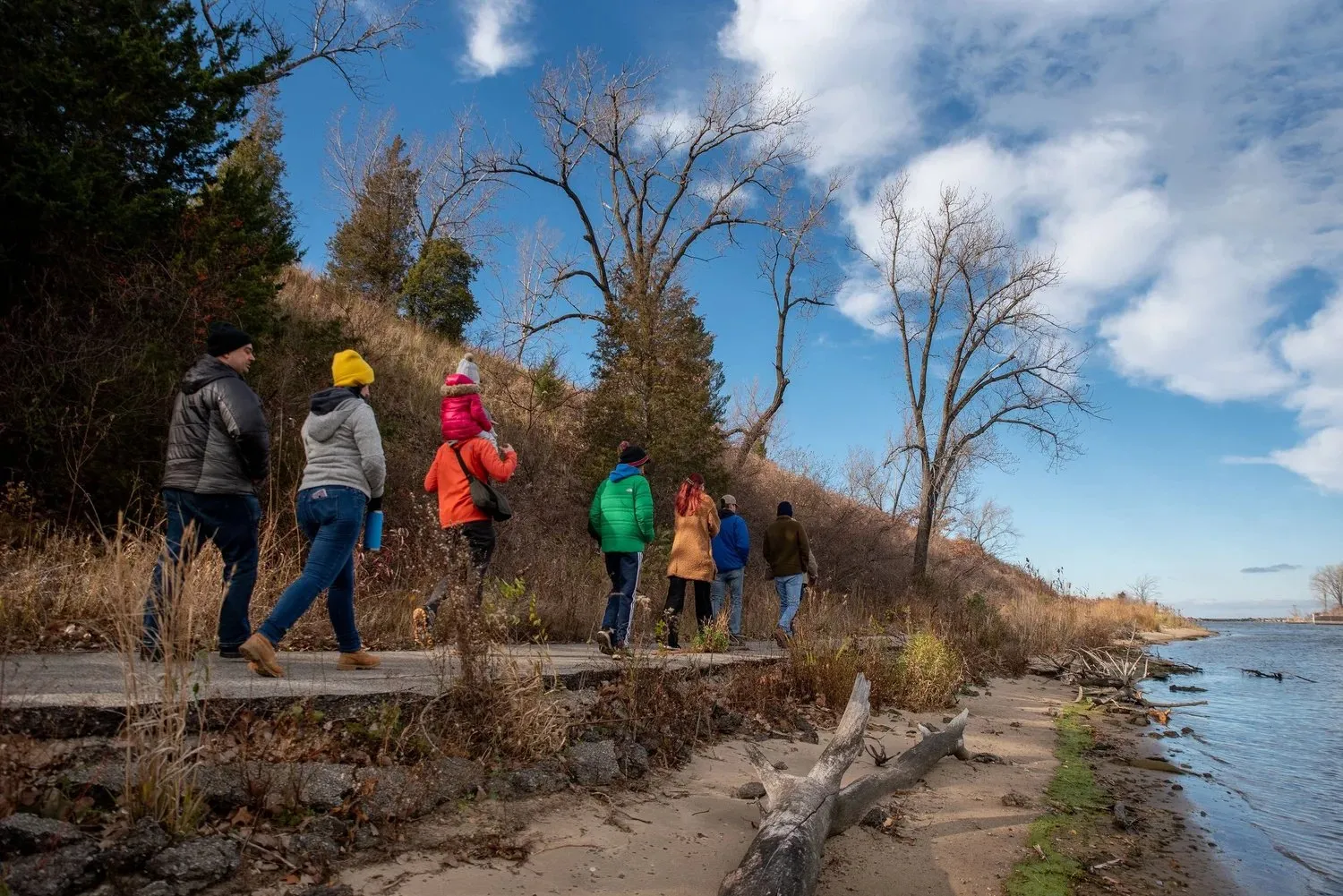 Group hiking a wooded lakeshore trail under a blue sky