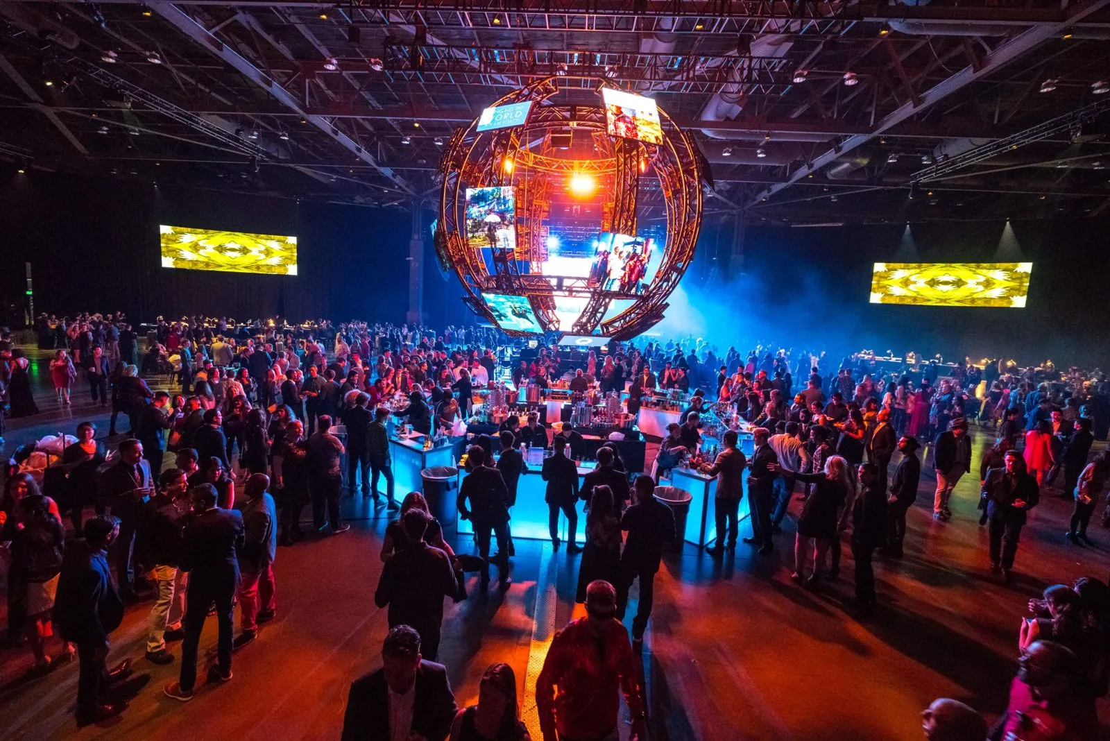 Crowd on a lit dance floor under a large illuminated sphere at a corporate event