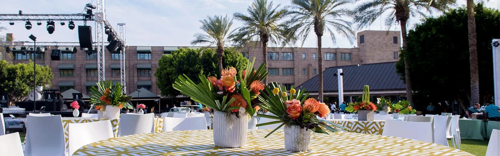 Outdoor event area with white lounge furniture, floral displays and palm trees in front of a resort