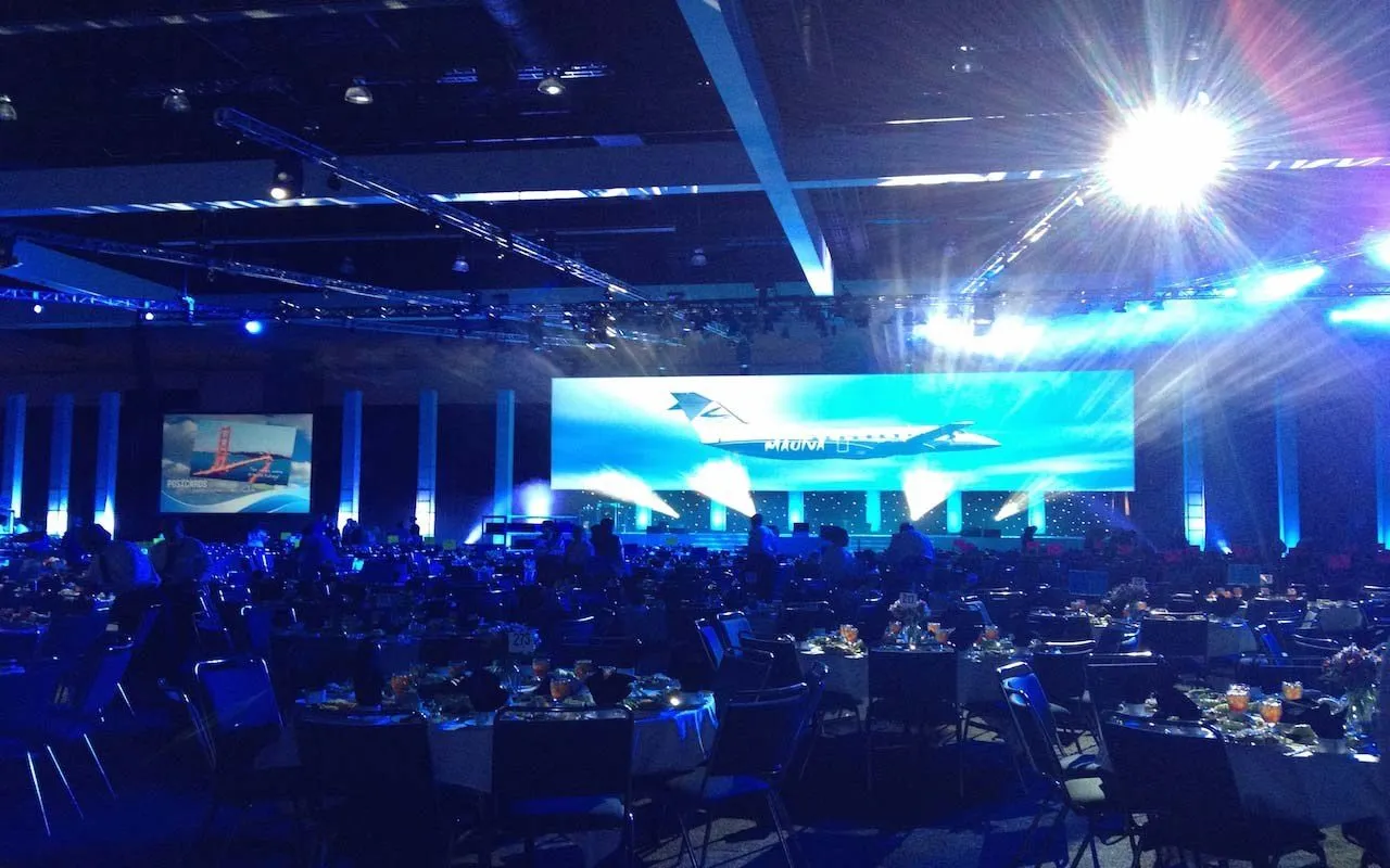Large evening general session with a wide stage screen and round tables