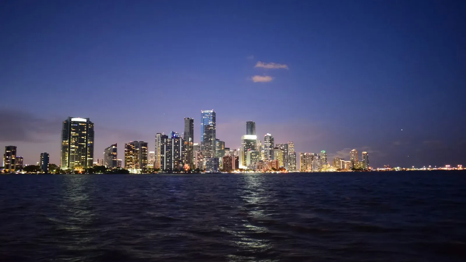 The Miami skyline lit up at dusk across the dark water of Biscayne Bay