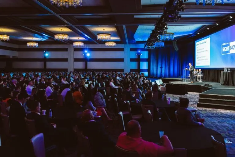 Attendees seated in a large conference hall facing the stage