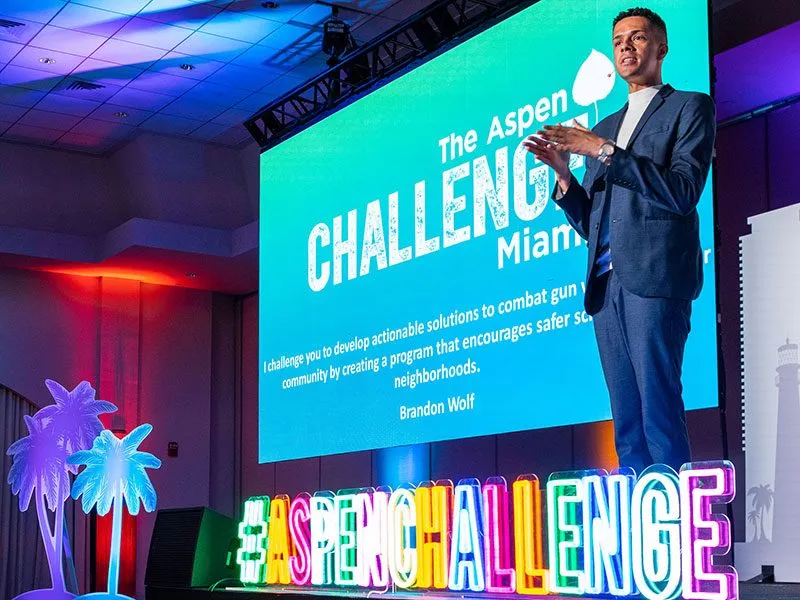 Speaker on stage in front of a large screen with lit letters