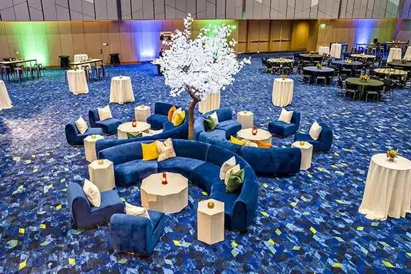 Event lounge with blue sofas, cocktail tables and a white floral tree on patterned carpet