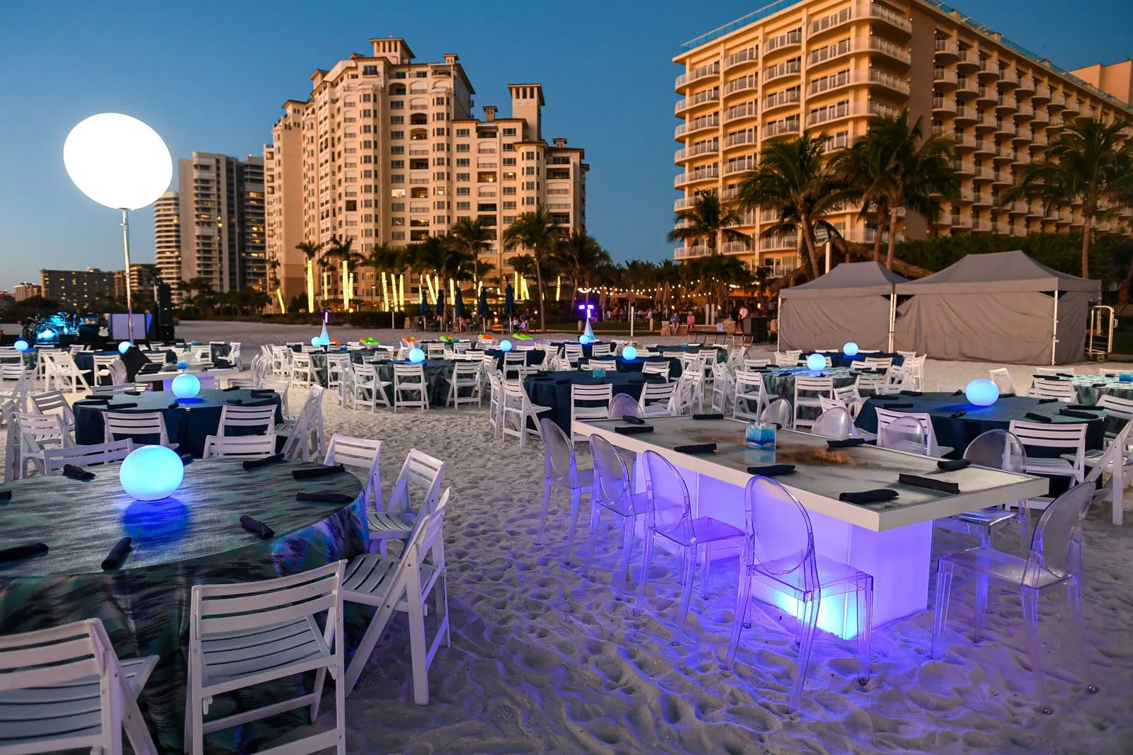 Evening beach reception with lit bars and lounge seating beside resort towers