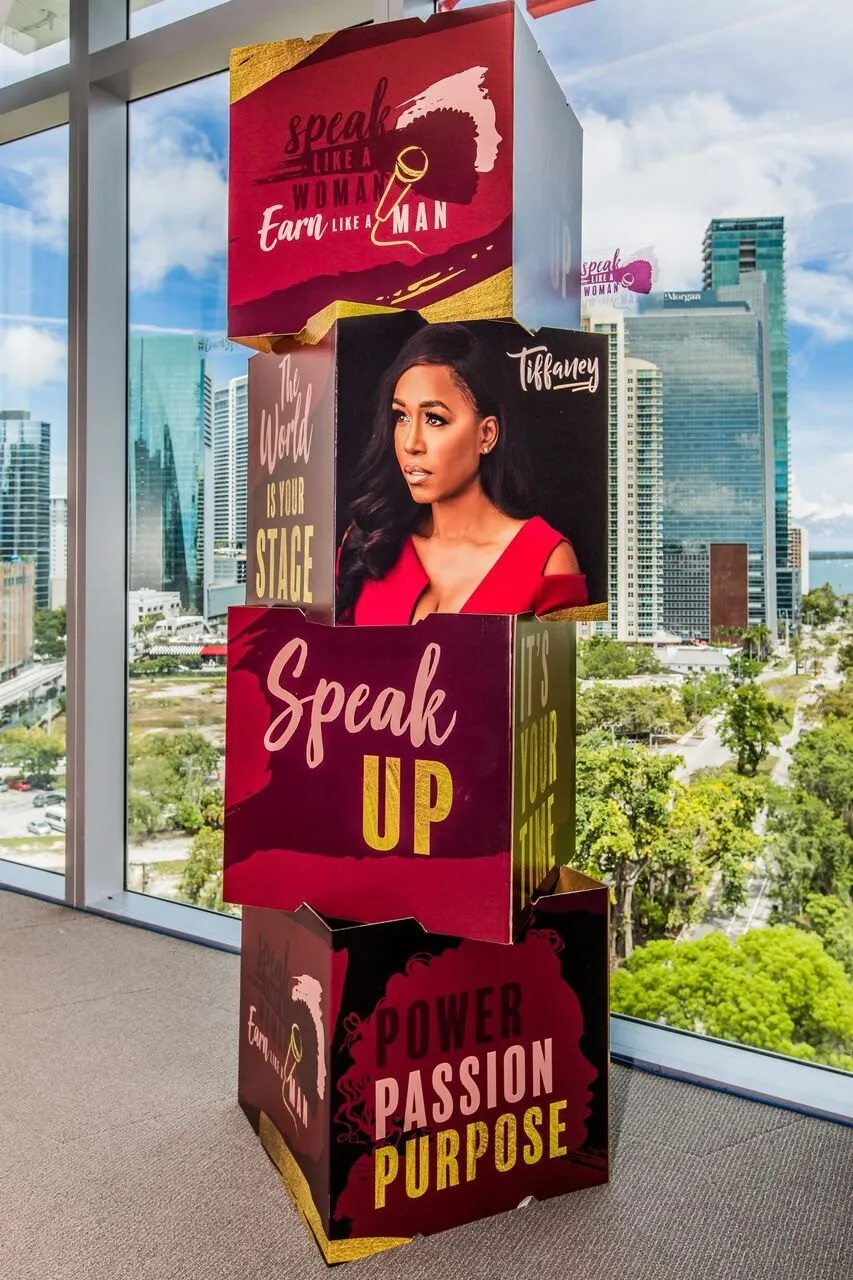 Branded Speak Up signage tower beside a window with a city view at the Speak Like a Woman Conference in Miami