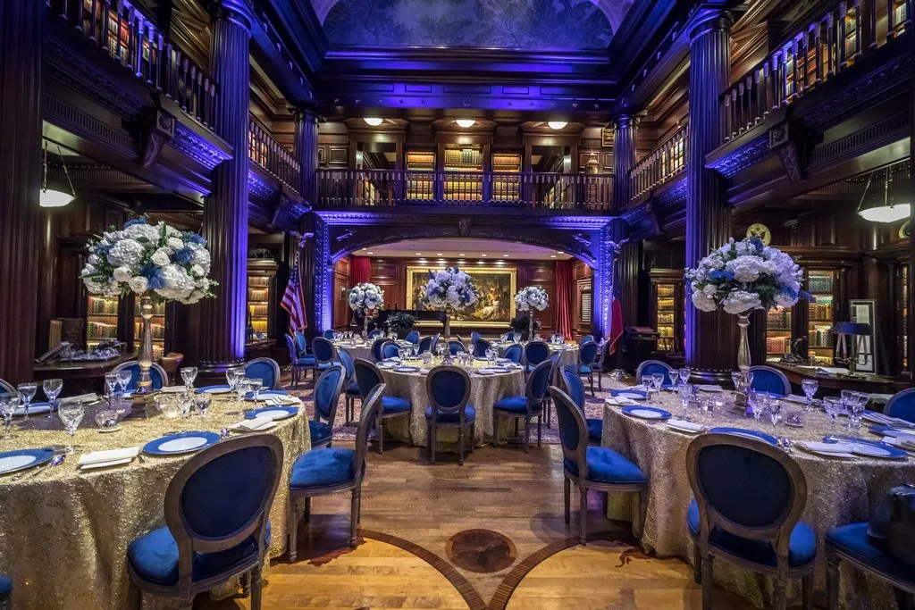Dinner tables with white florals set in a wood-paneled library for the executive retreat
