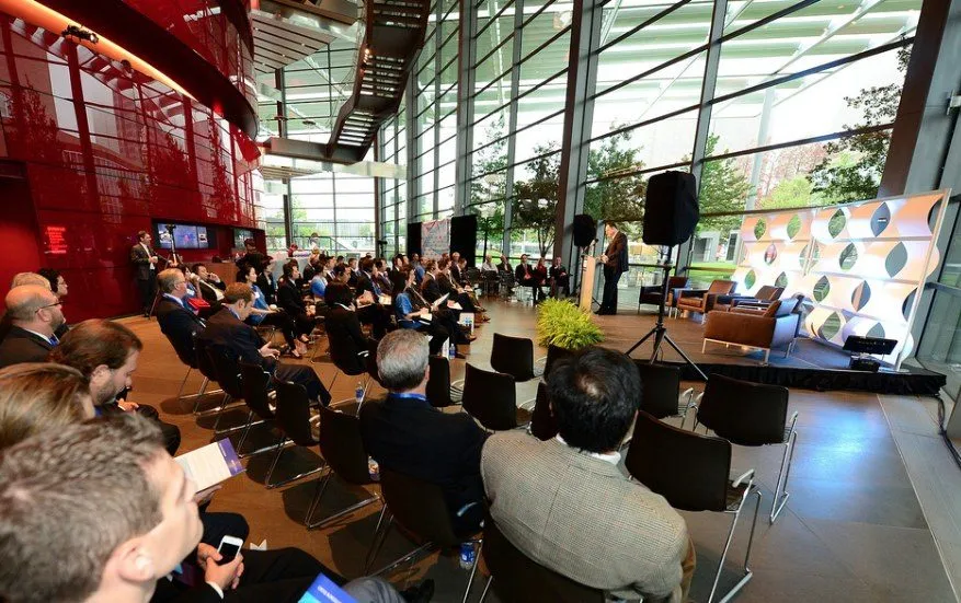Seated audience at a daytime conference session with a stage and panel