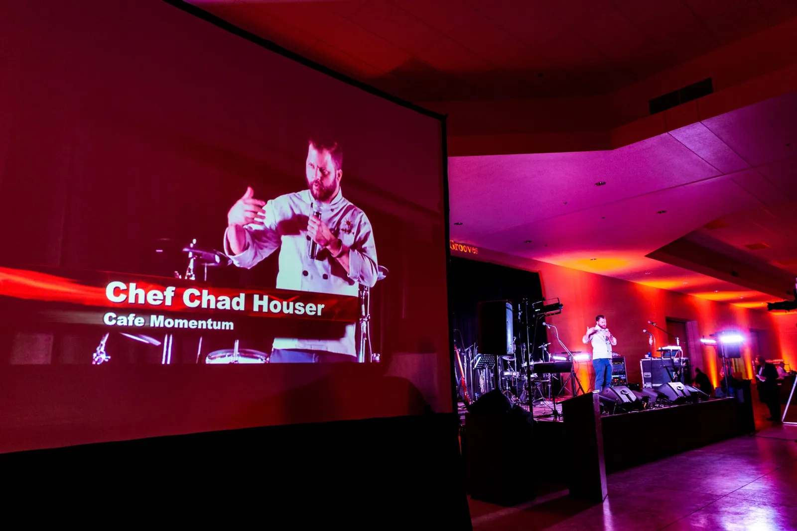 Speaker shown on a large projection screen with red stage lighting