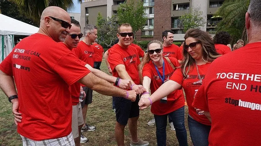 Team members in red shirts joining hands in a circle outdoors
