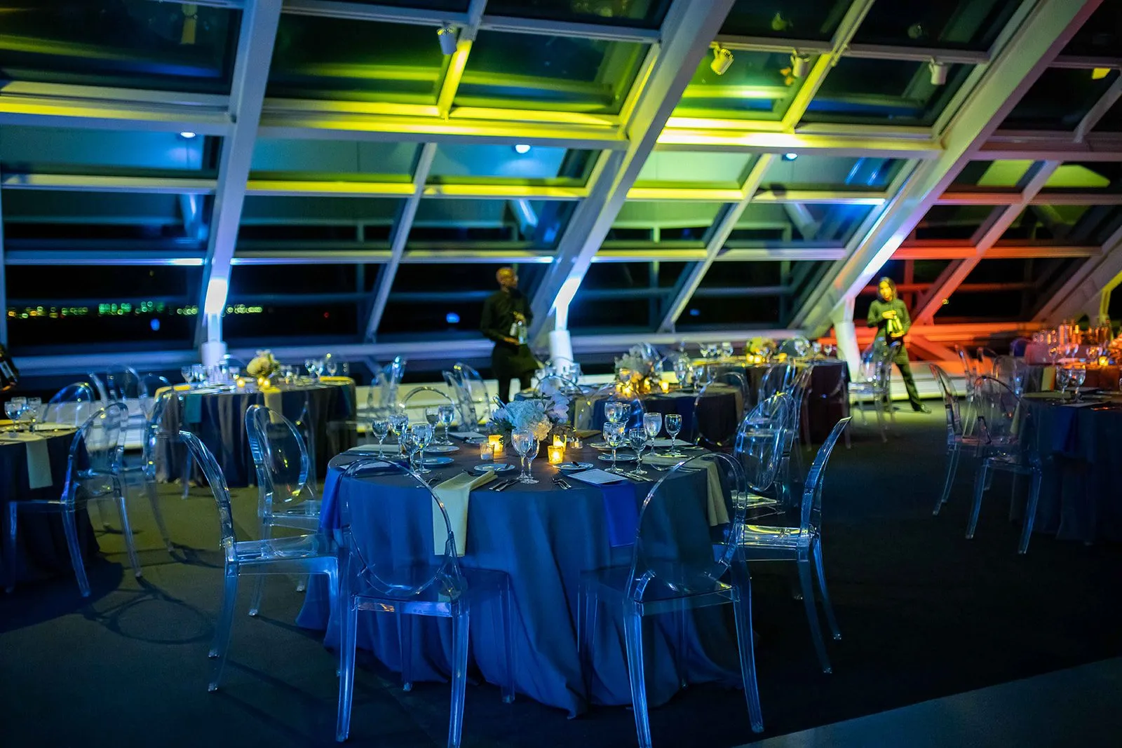 Dinner tables under a glass ceiling lit in colored light at a corporate event