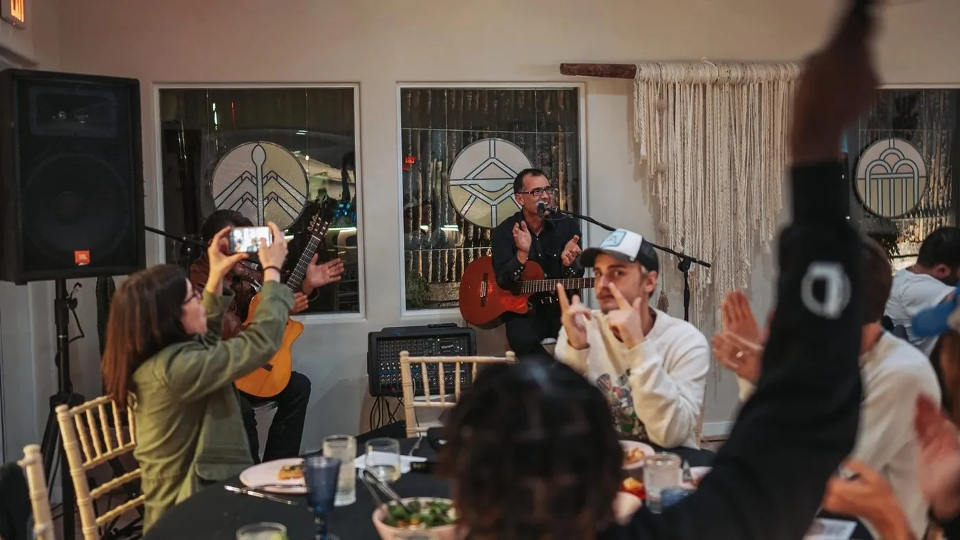 Team members seated at a dinner table with a guitarist playing in the room
