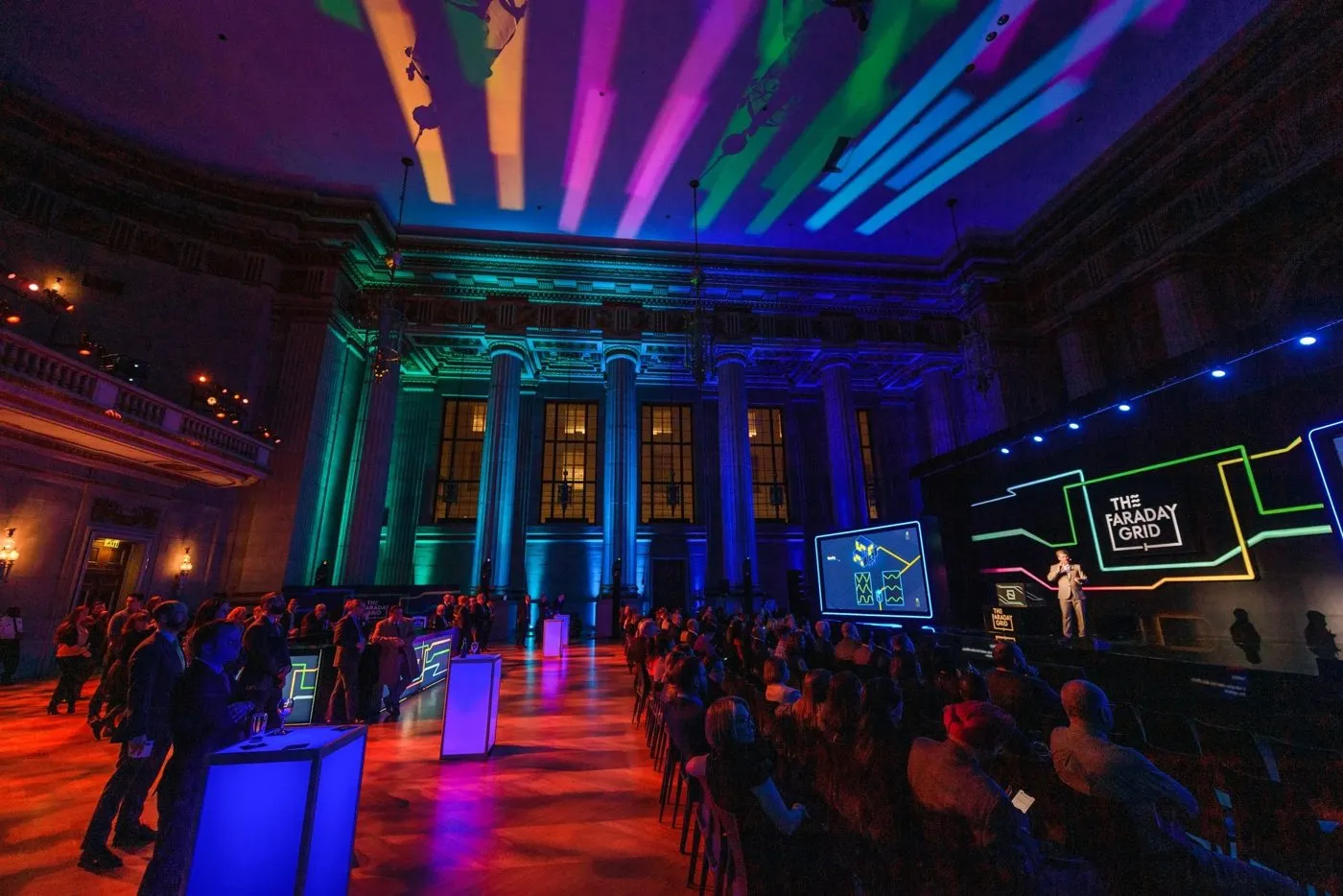 Large hall with colorful ceiling lighting, seated audience and stage screens