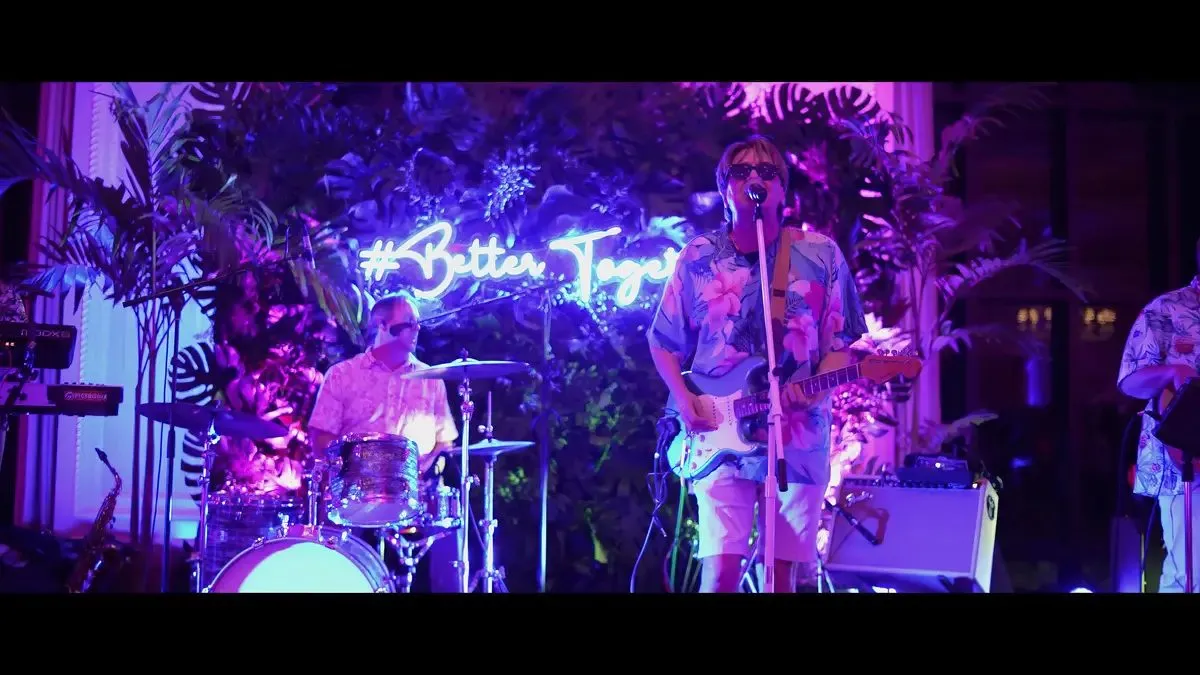 Band on a stage with neon lights and palm decor at an evening event