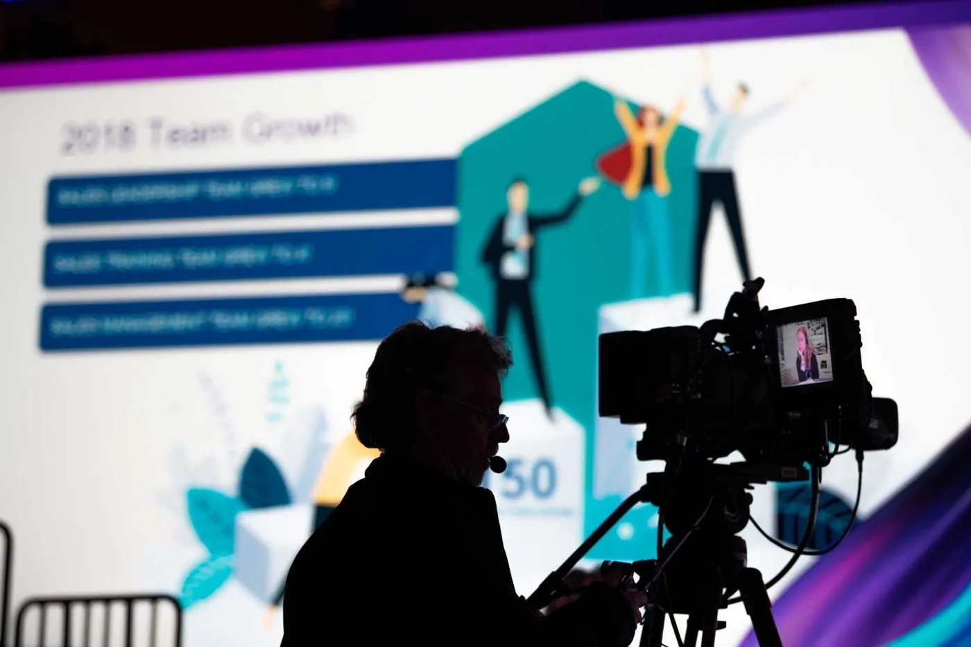 Camera operator in silhouette filming a presentation screen at a corporate event