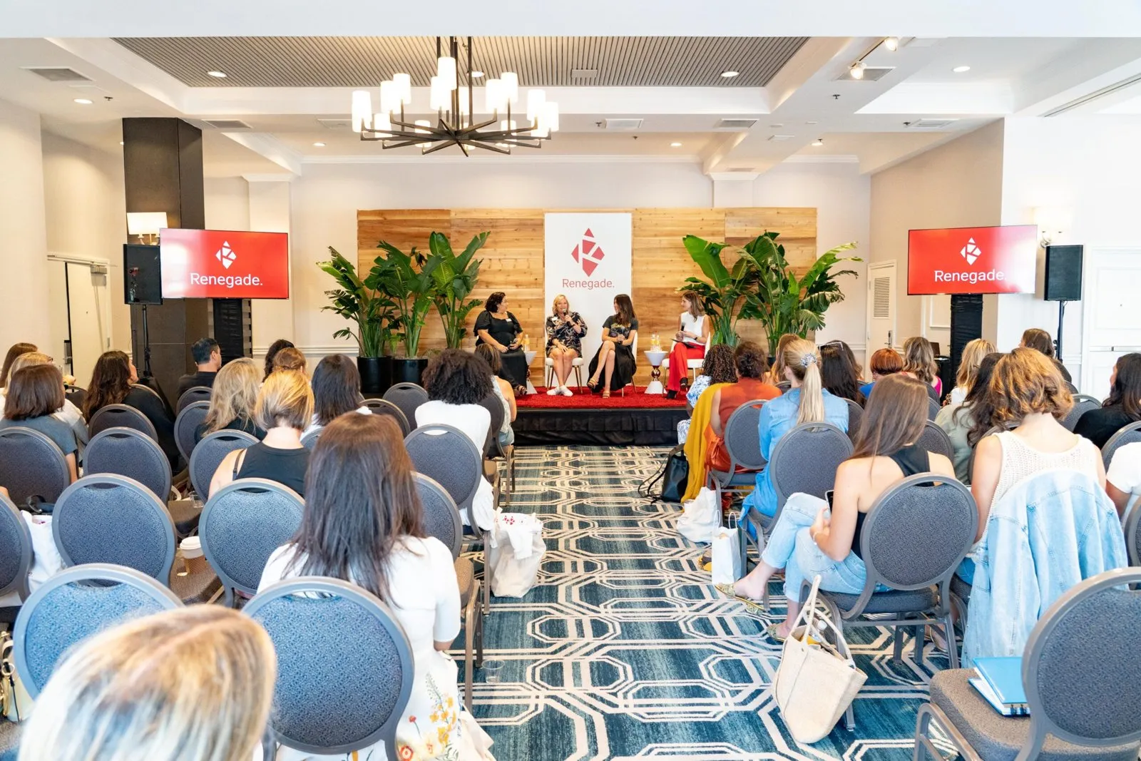 Audience seated for a panel discussion on a stage in a hotel meeting room