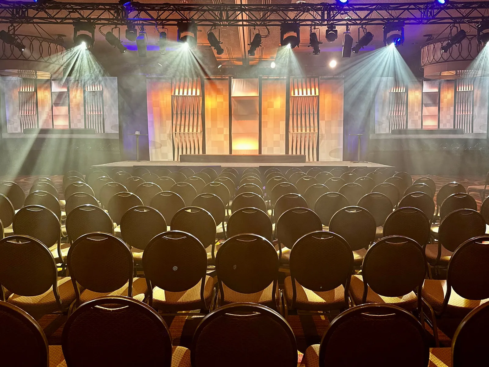 Ballroom stage with scenic panels and lighting above rows of chairs
