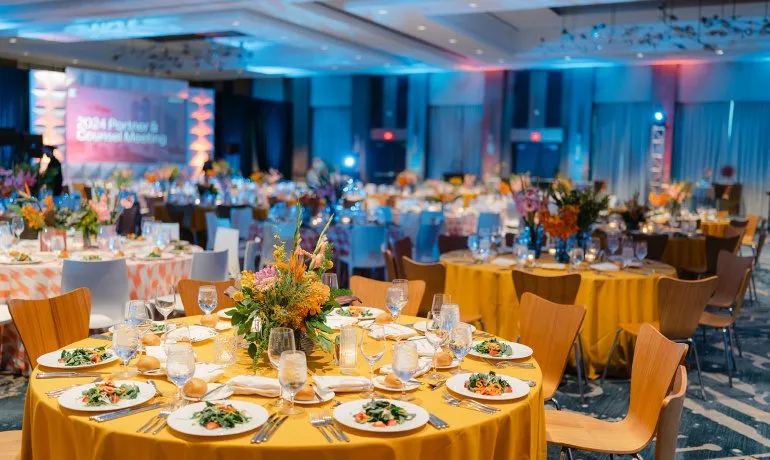 Round tables with gold linens and floral centerpieces set for an annual conference dinner