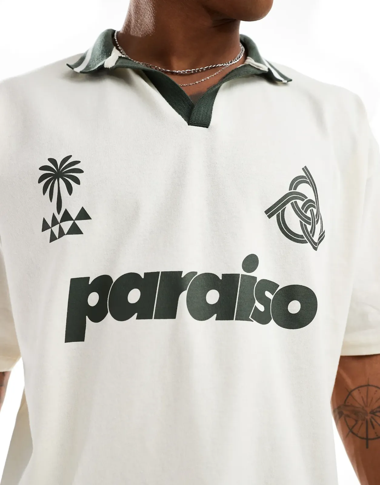 A cream knit sports shirt with a dark green striped open collar, printed with a palm tree crest, an interlocking knot emblem and a large word across the chest