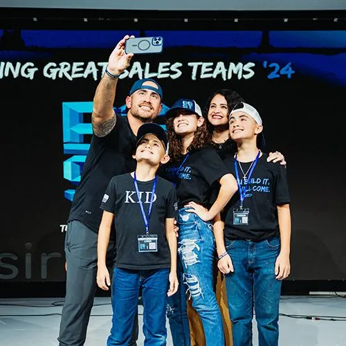 Team members posing on a stage in front of a sales conference screen