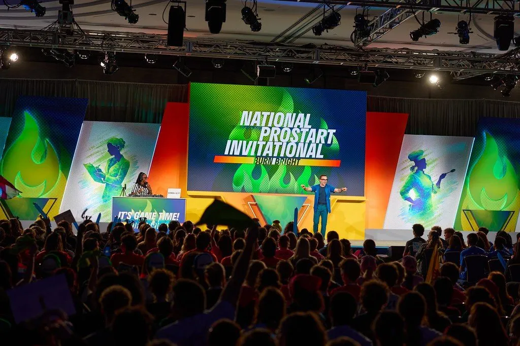 Audience facing a large conference stage with branded video screens