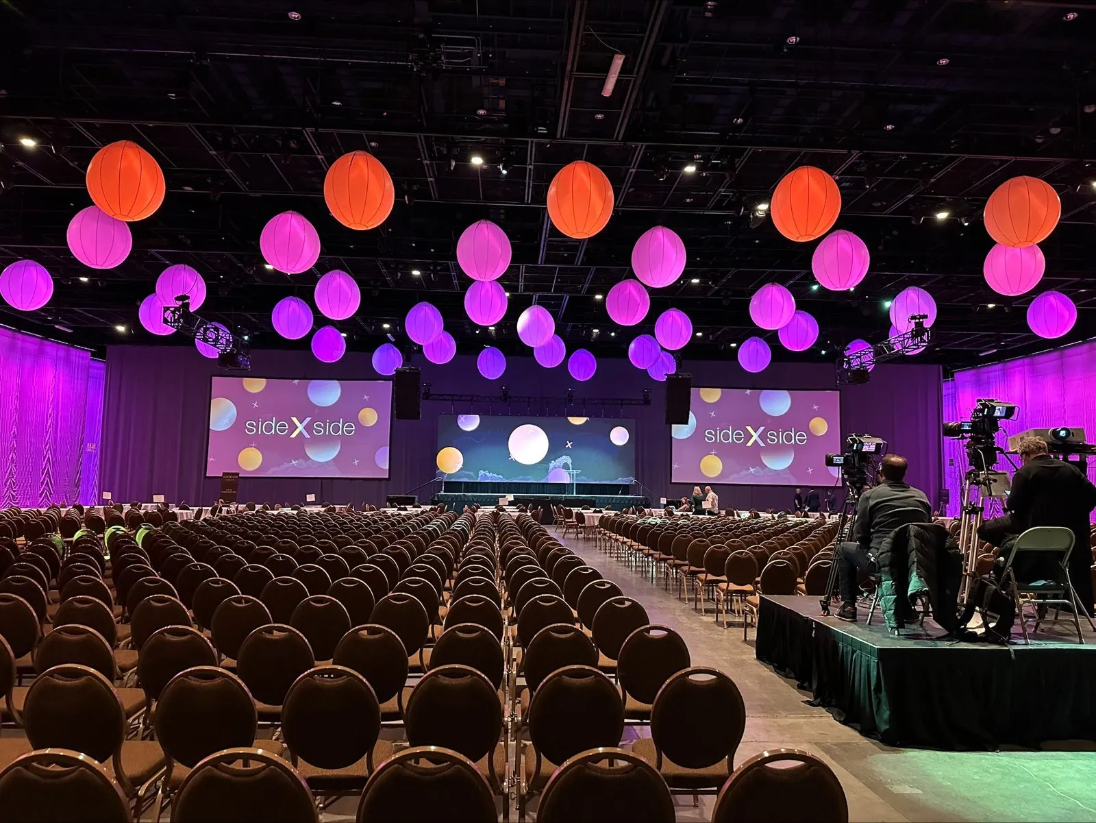 General session room with rows of chairs, stage and lit decor spheres