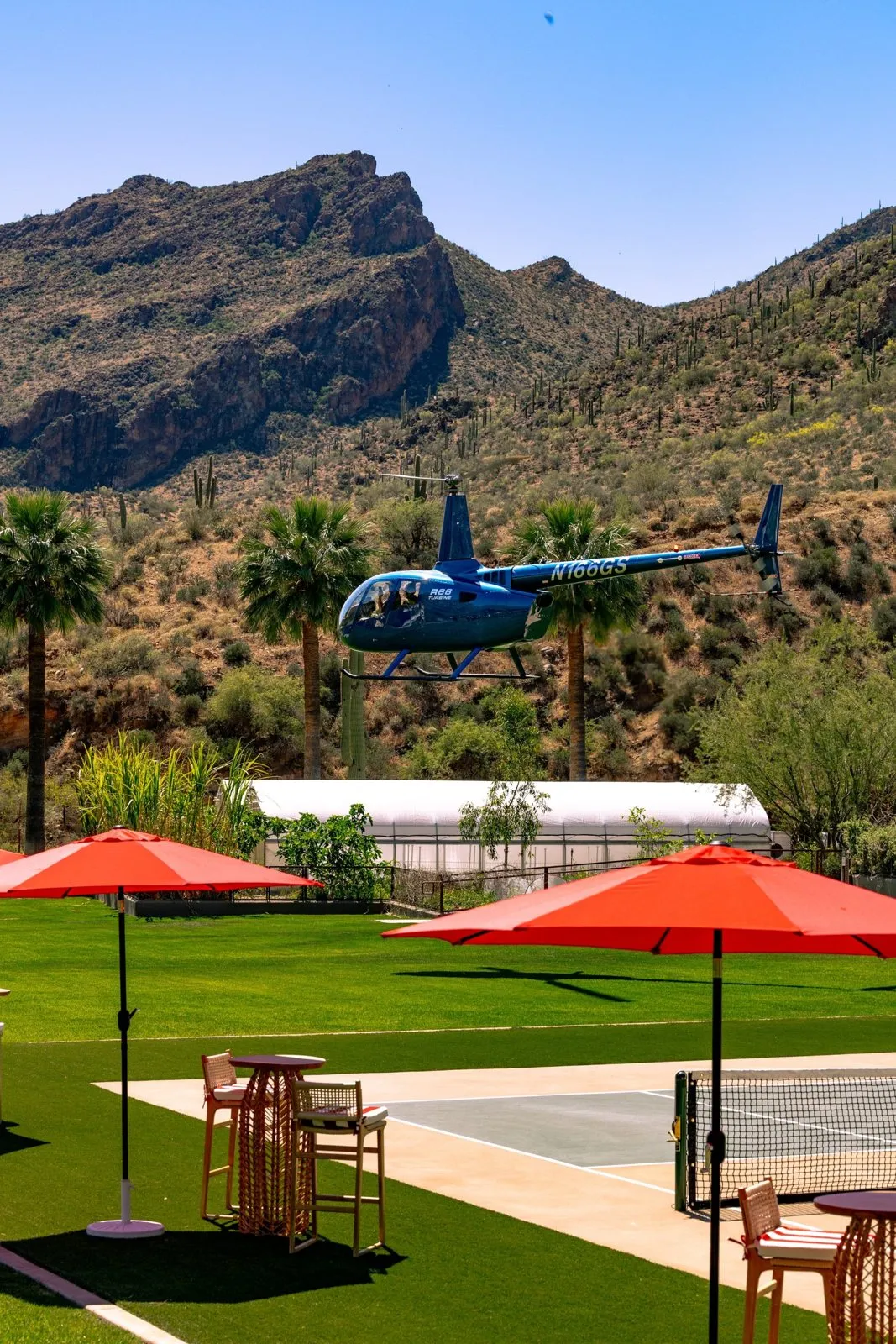Helicopter flying over a lawn with red umbrellas and a desert canyon behind at Castle Hot Springs