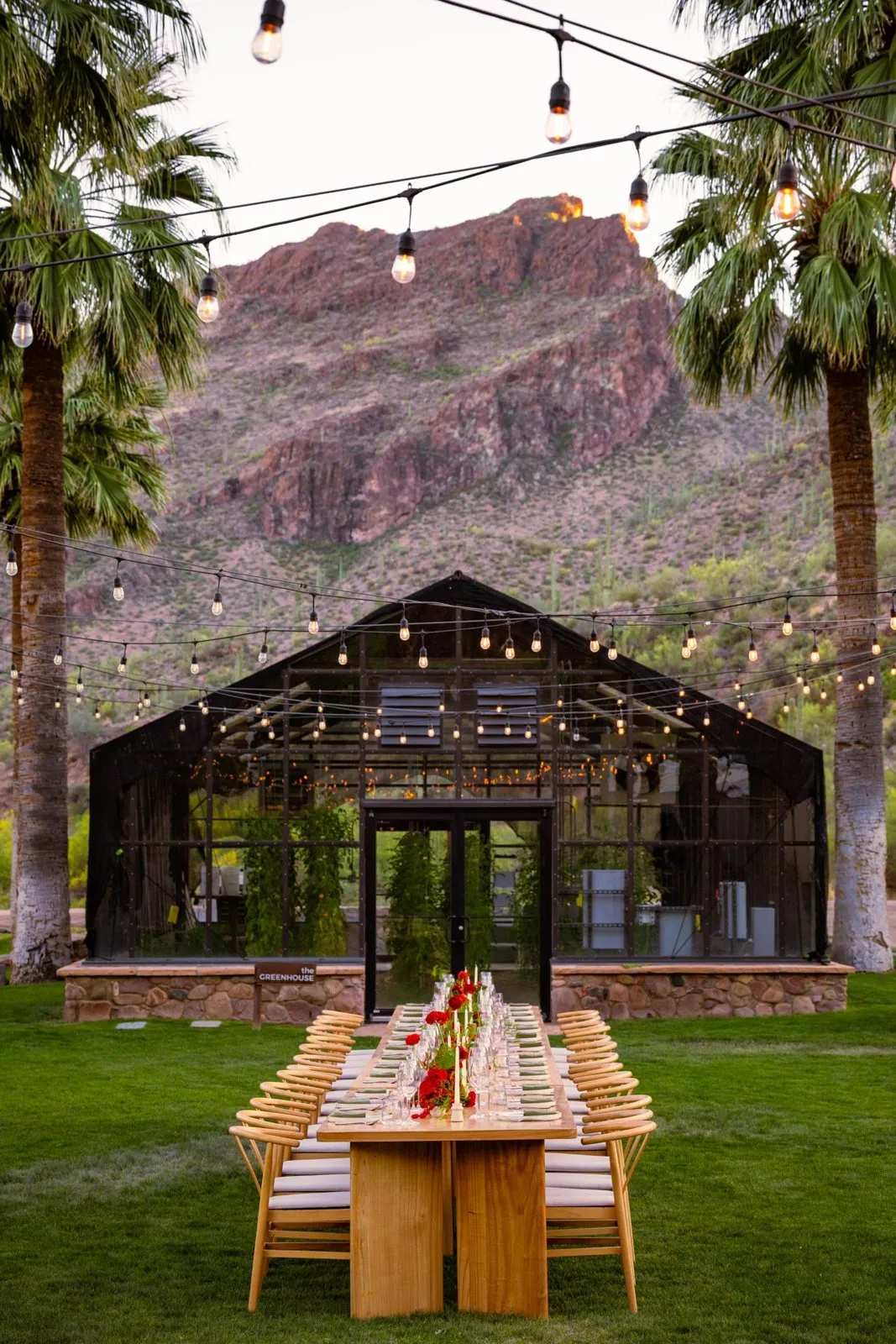 Long dinner table set in front of a glass greenhouse and red rock cliffs