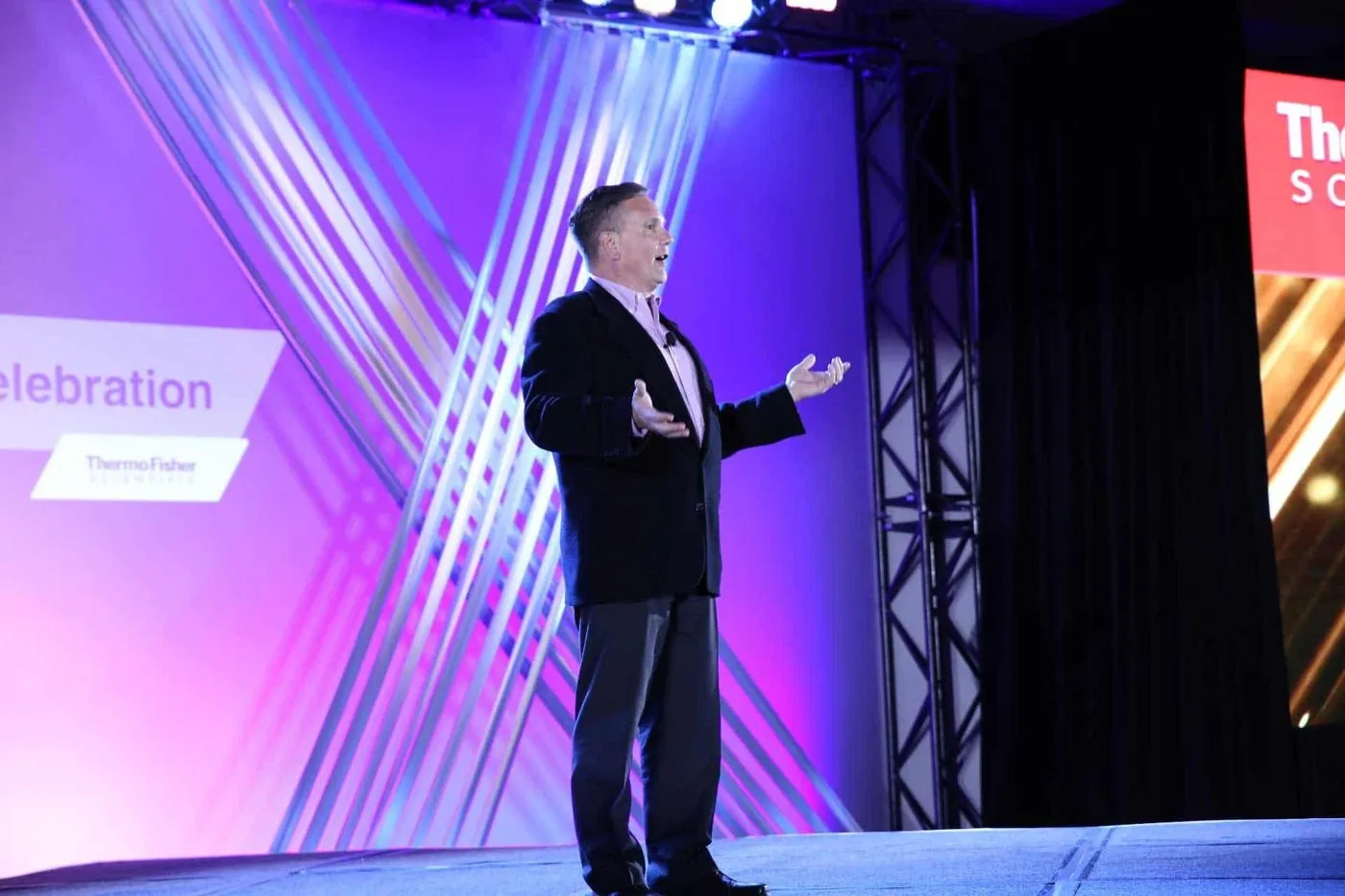 Speaker on stage in front of a purple LED backdrop at a corporate meeting