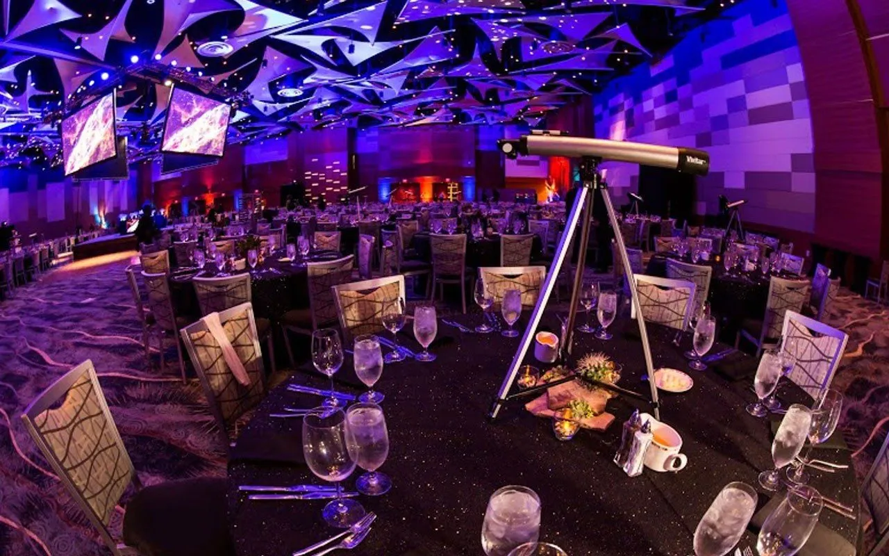 Space themed reception with a telescope and dinner tables under purple lighting