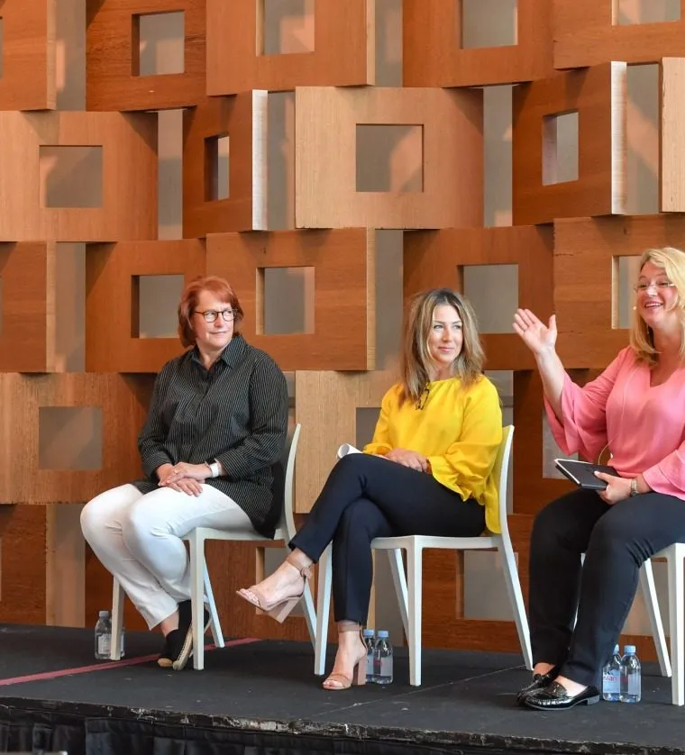 Three panelists seated on a wood paneled conference stage