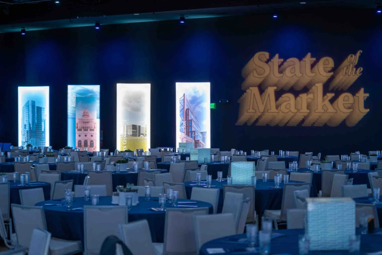Ballroom with round tables and a lit stage backdrop for an annual market meeting