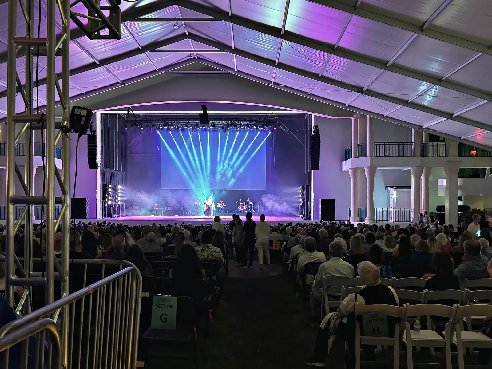 Lit stage under a tent roof with a seated audience