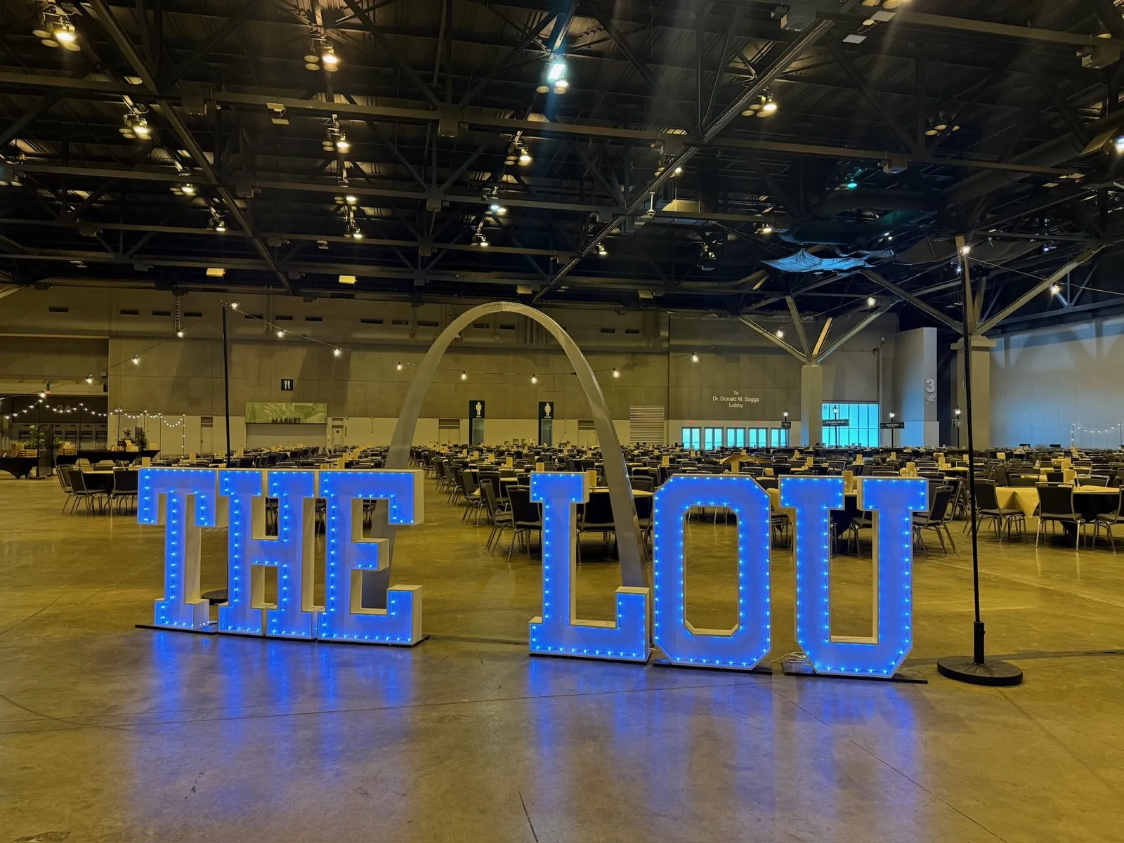 Illuminated THE LOU letters in front of a Gateway Arch graphic in an exhibition hall