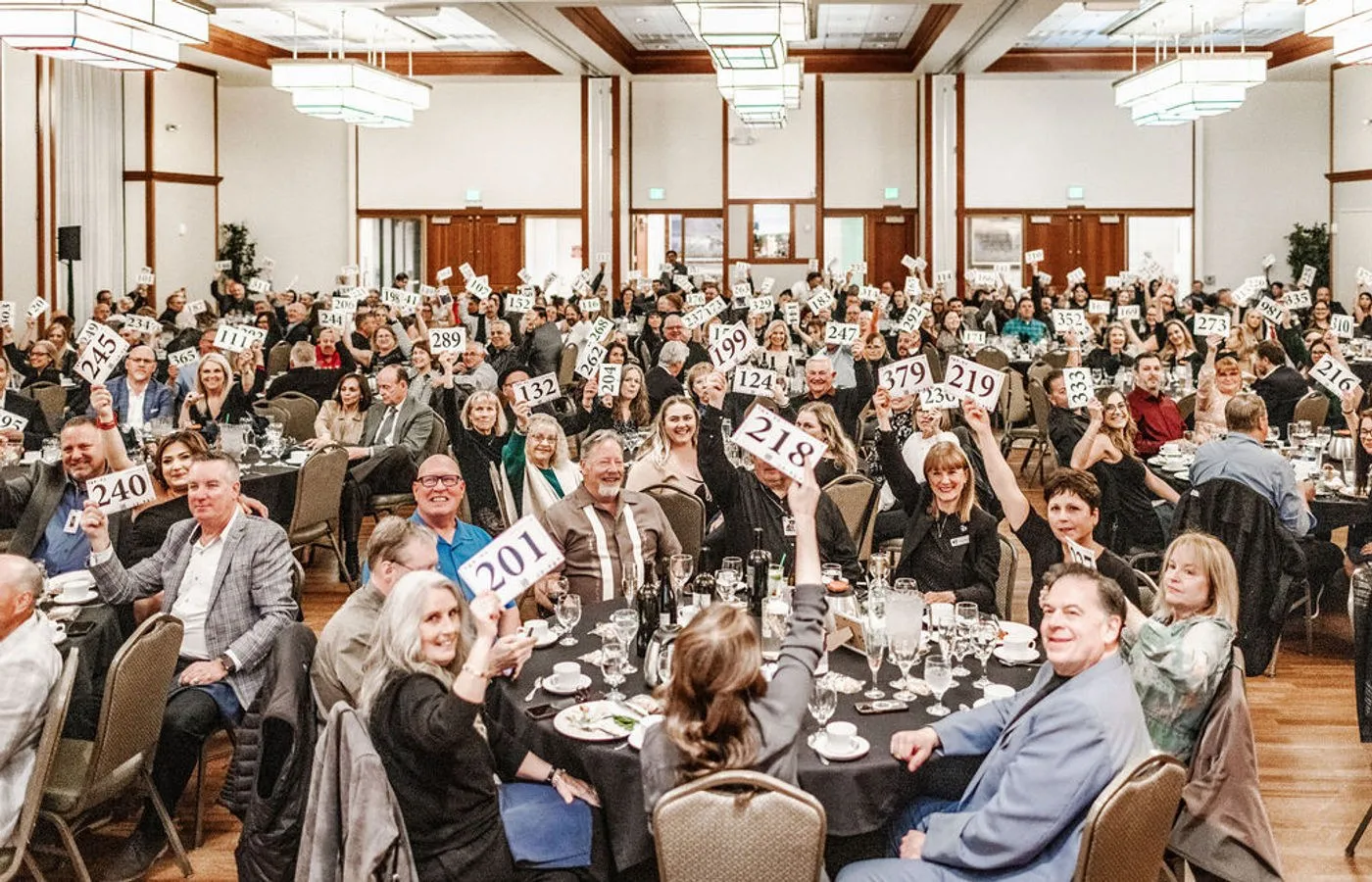 Full banquet room of guests at dinner tables raising paddles at a gala