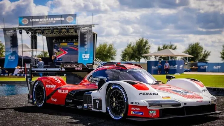 Race car on display at an outdoor brand activation with a stage and tents
