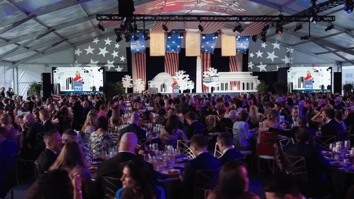 Large gala dinner crowd seated under a tent with stage screens