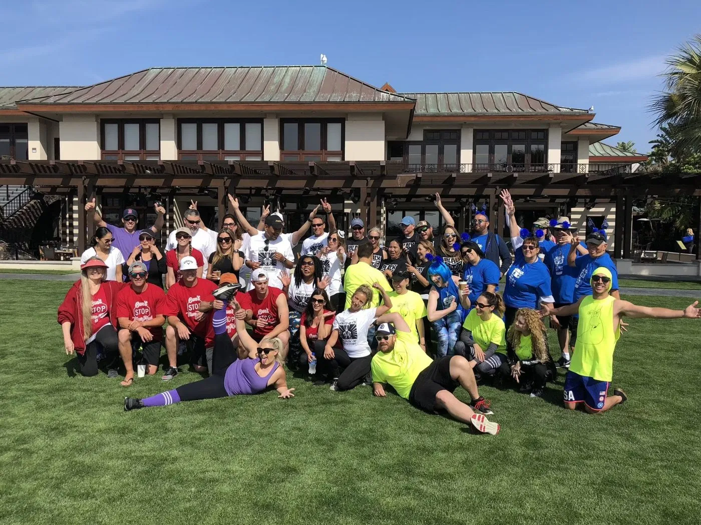 Large group in matching colored shirts posing on a lawn in front of a building