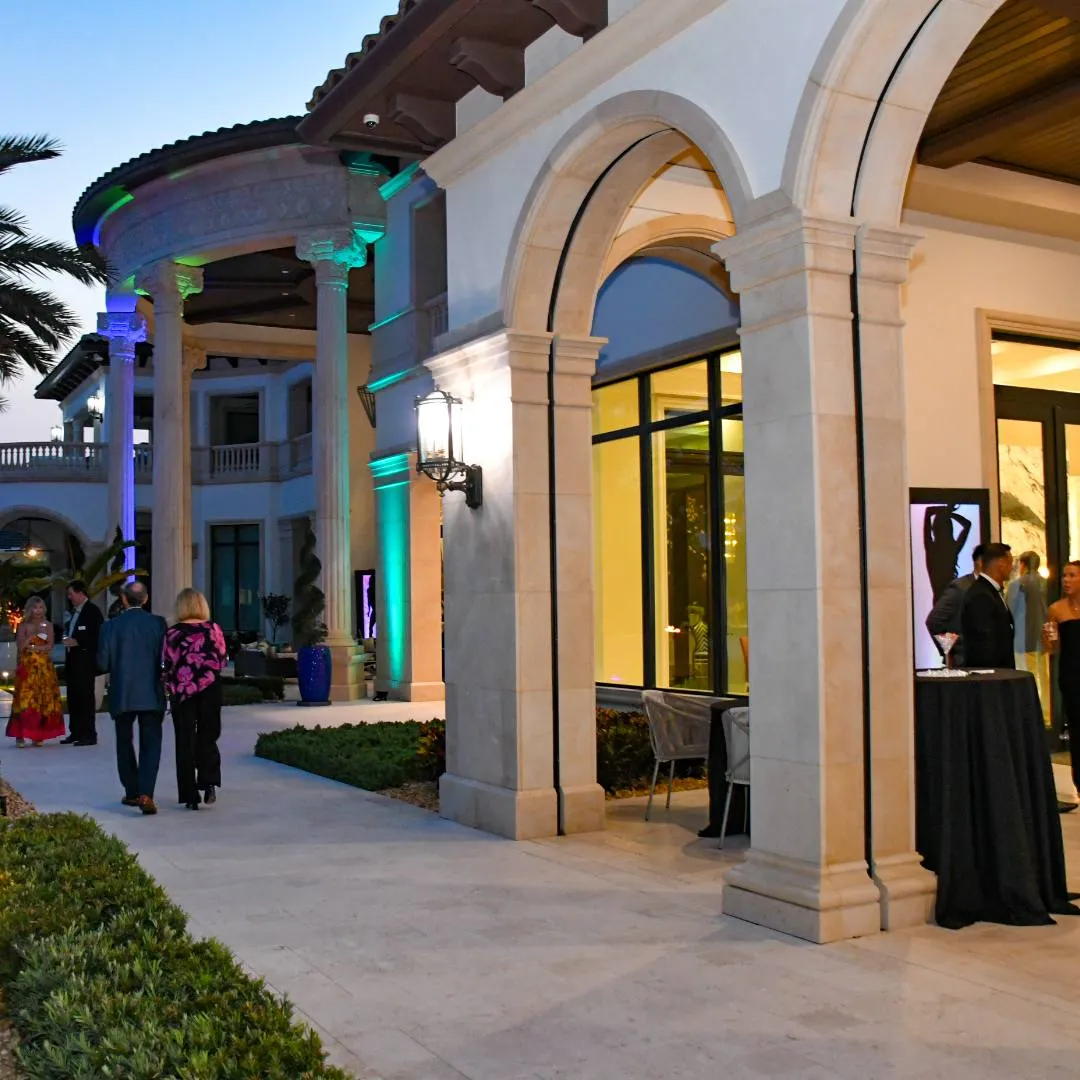 Guests on an arched, uplit terrace at dusk with cocktail tables, Impact 100 Men charity event, May 2024