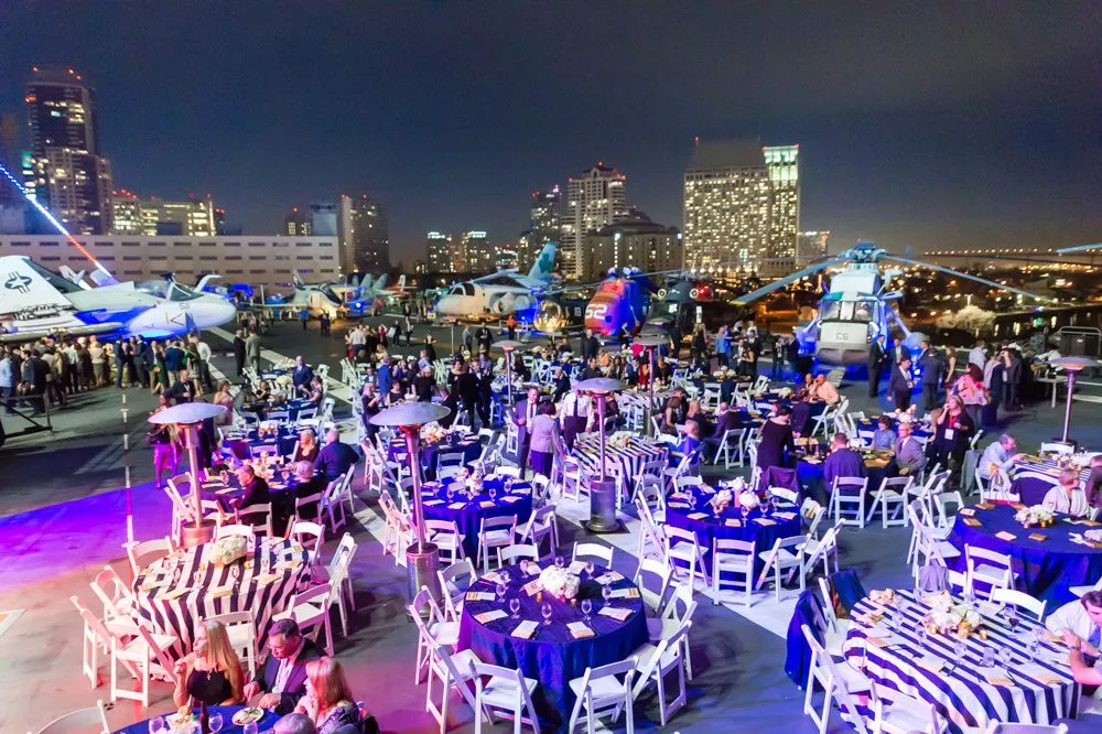 Evening group event with guests at round tables beside a city skyline at a museum venue