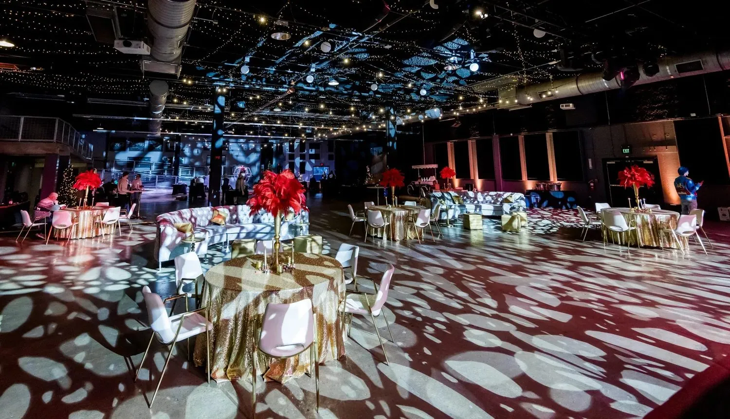Ballroom set with round tables and red floral centerpieces under patterned lighting