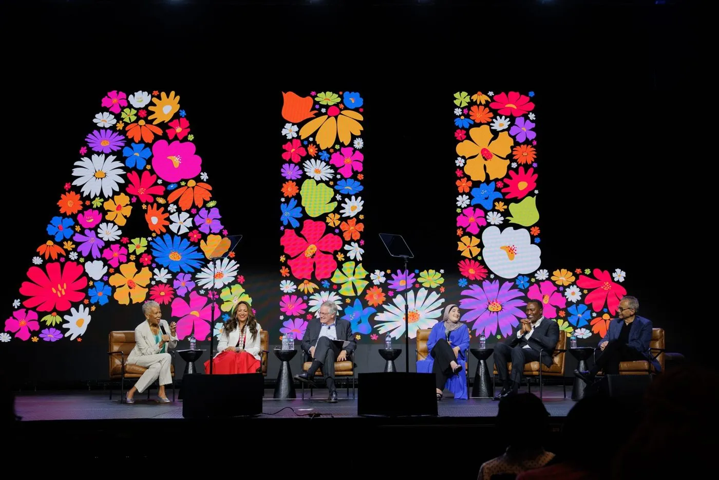 Panel on a dark stage framed by a large floral lettering backdrop
