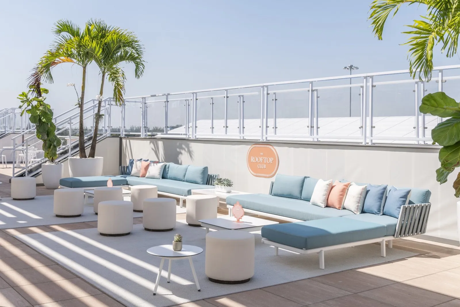 Rooftop lounge with blue sofas, palm trees and umbrellas at the Paddock Club