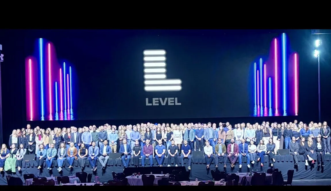 Summit attendees gathered on stage under a lit logo at Chelsea Theater, Las Vegas