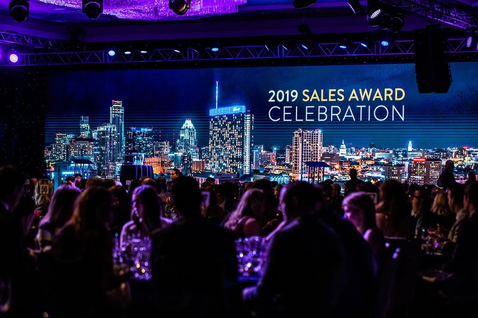 Audience facing a lit stage screen at a corporate sales celebration dinner