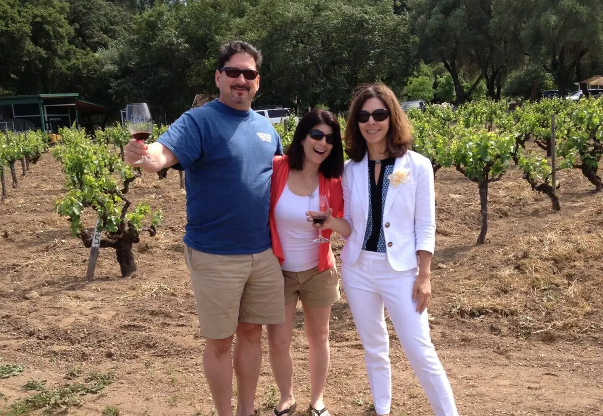 Three guests holding wine glasses in a vineyard